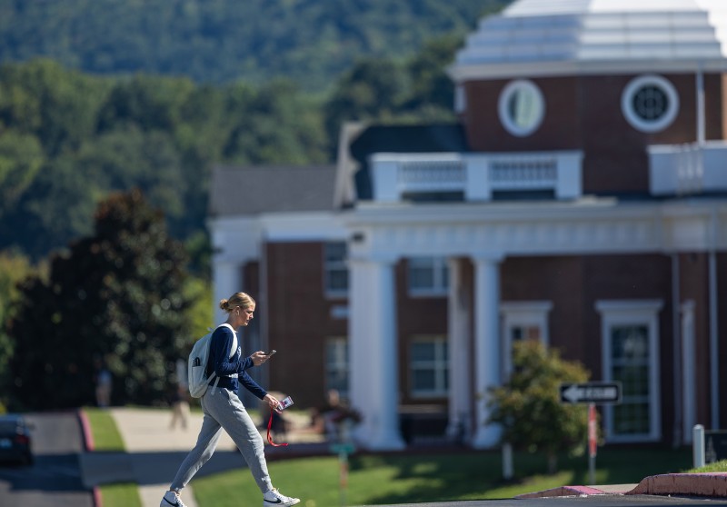 A student walks on campus in front of the science building. 