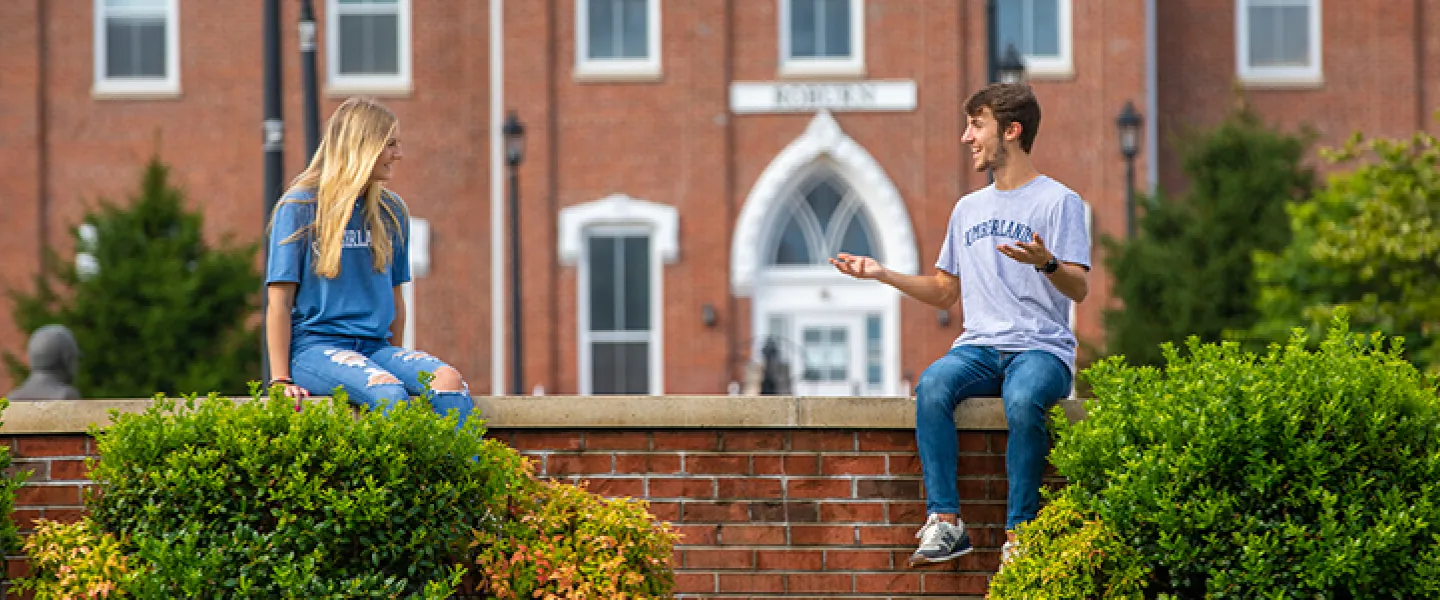 Two students sitting on a wall outside