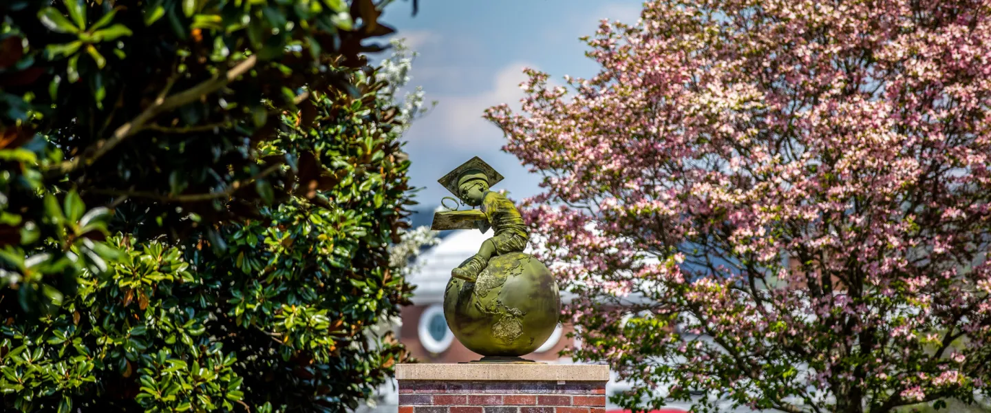 Bronze statue of a boy studying while seated on a globe