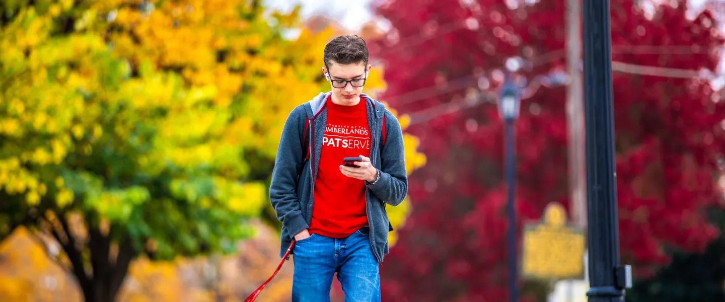 A student looking at their phone while walking