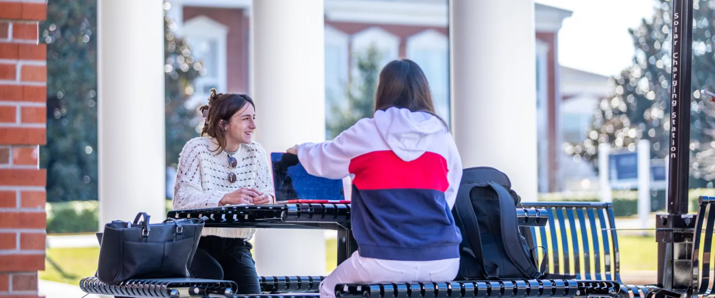 Two students seated at a table ouside