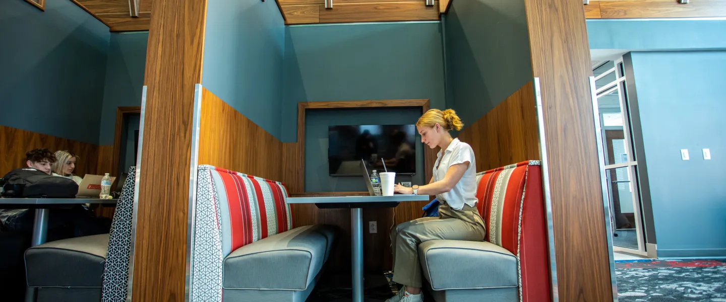 A student sitting in a booth and using a laptop
