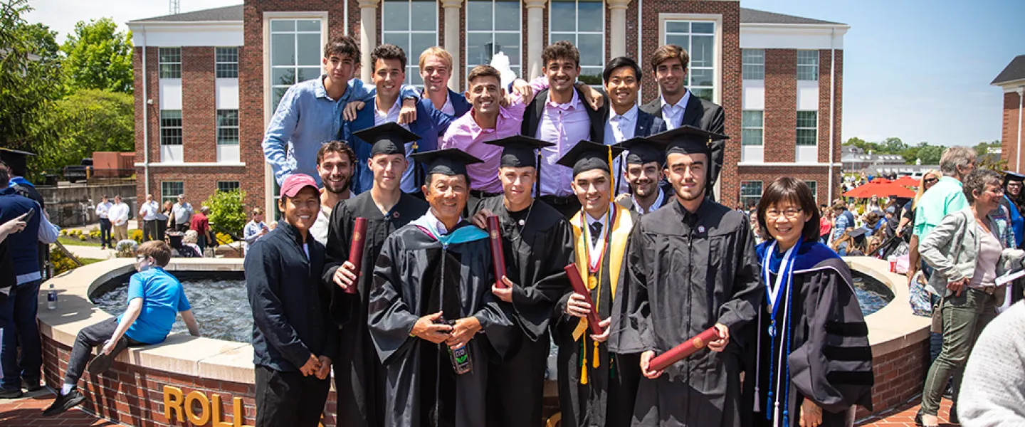 Students wearing cap and gown with friends behind