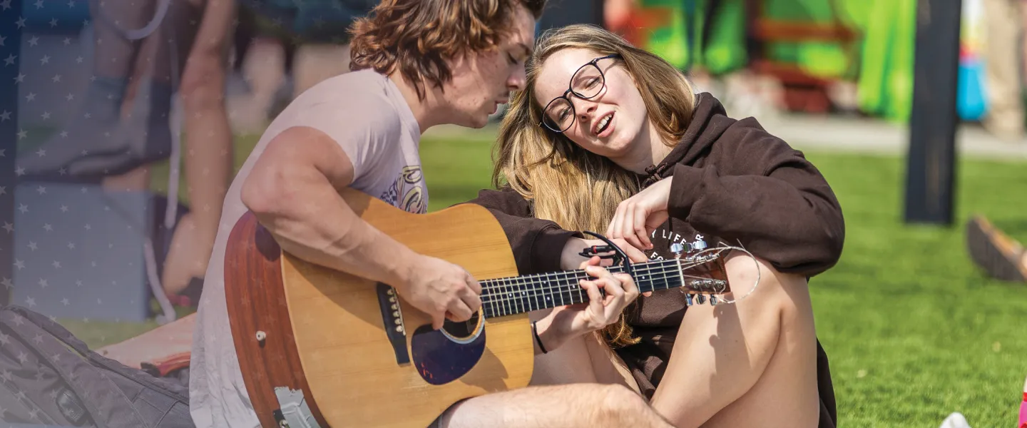 Two students play guitar and sing on campus. 
