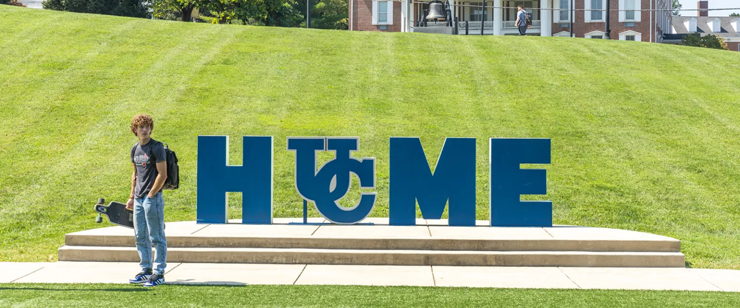 A student stands with a skateboard near Cumberlands HOME sign.