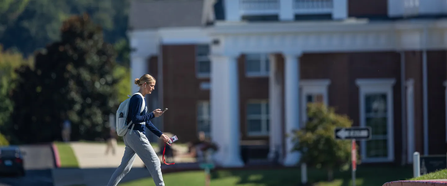 A student walks on campus in front of the science building. 