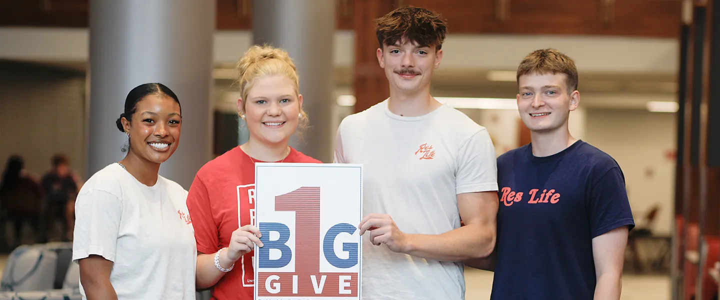 Students hold a sign promoting give day. 