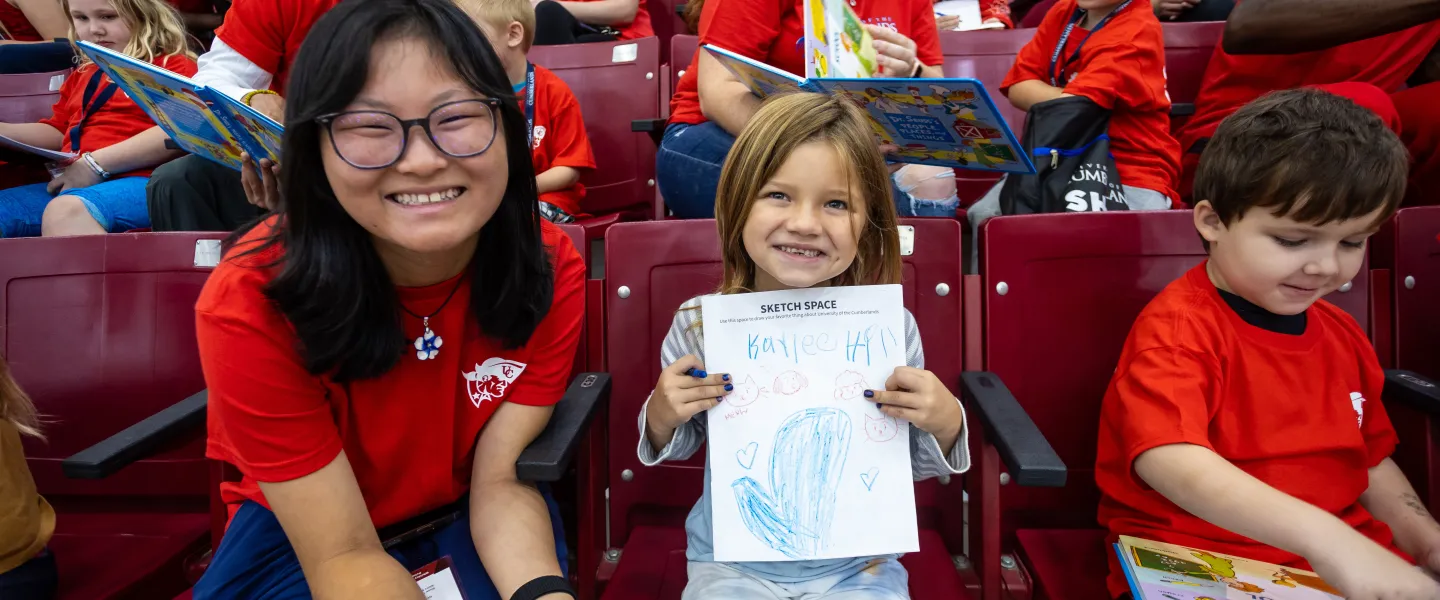An international student helps an elementary student with a coloring. 