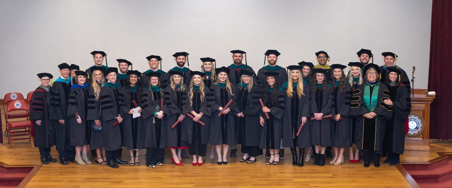 The first graduating class from the DPT program post on stage for a photo. 