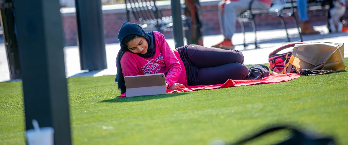 A female student relaxes on campus while using a computer. 