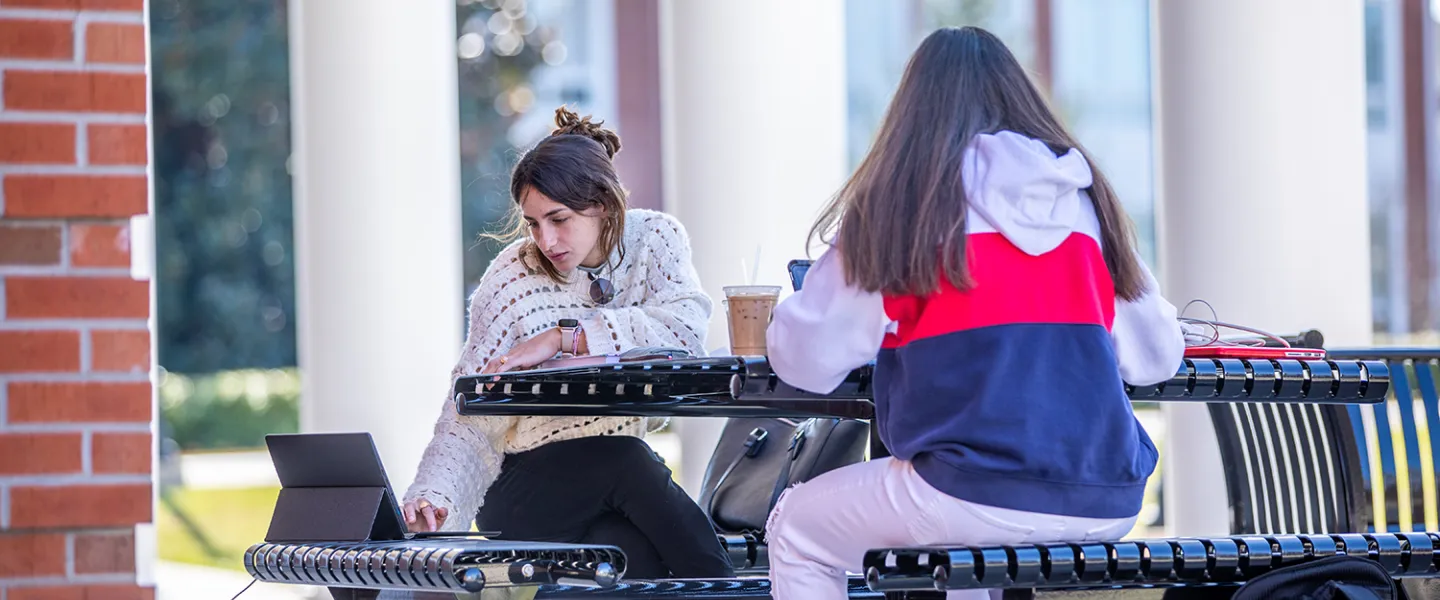 Two girls studying outside on a bench. 