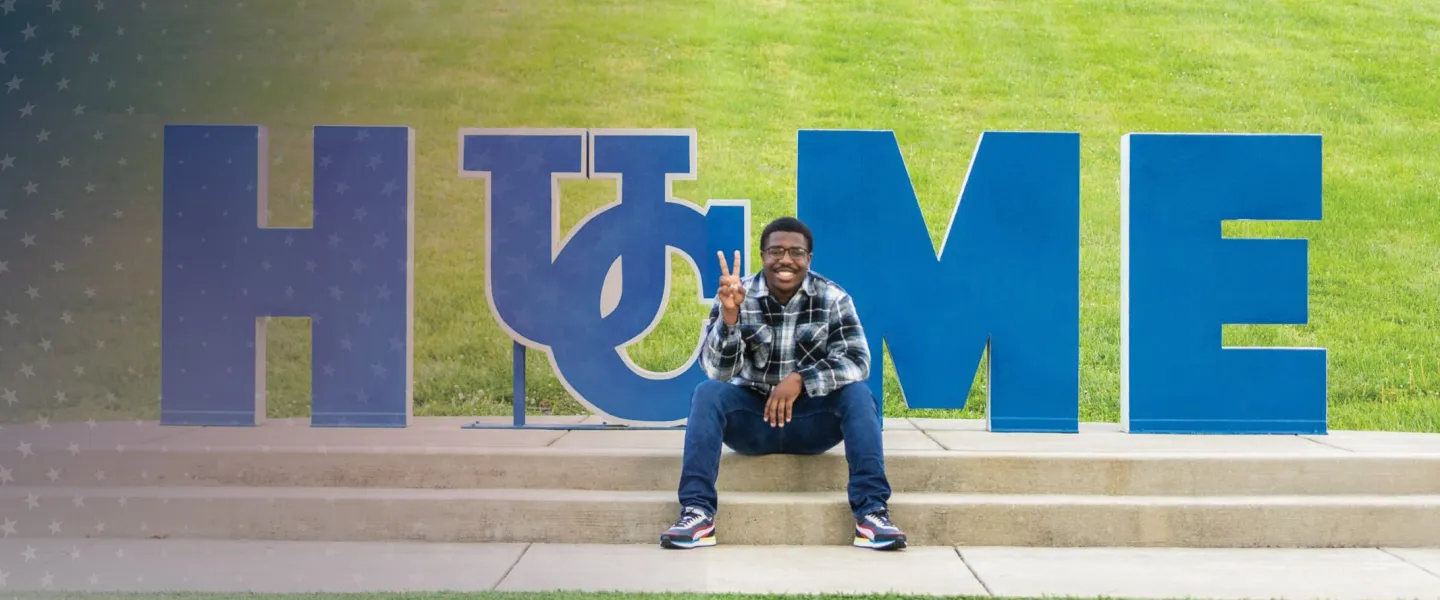 A student sits by the Home sign on campus.