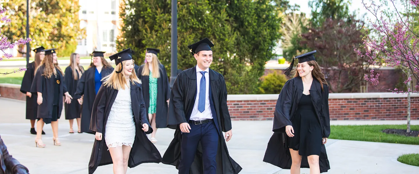 Graduates walk across the campus quad. 