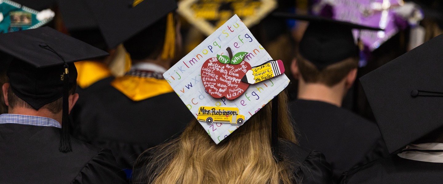 A decorated graduation hat with a teacher motif. 