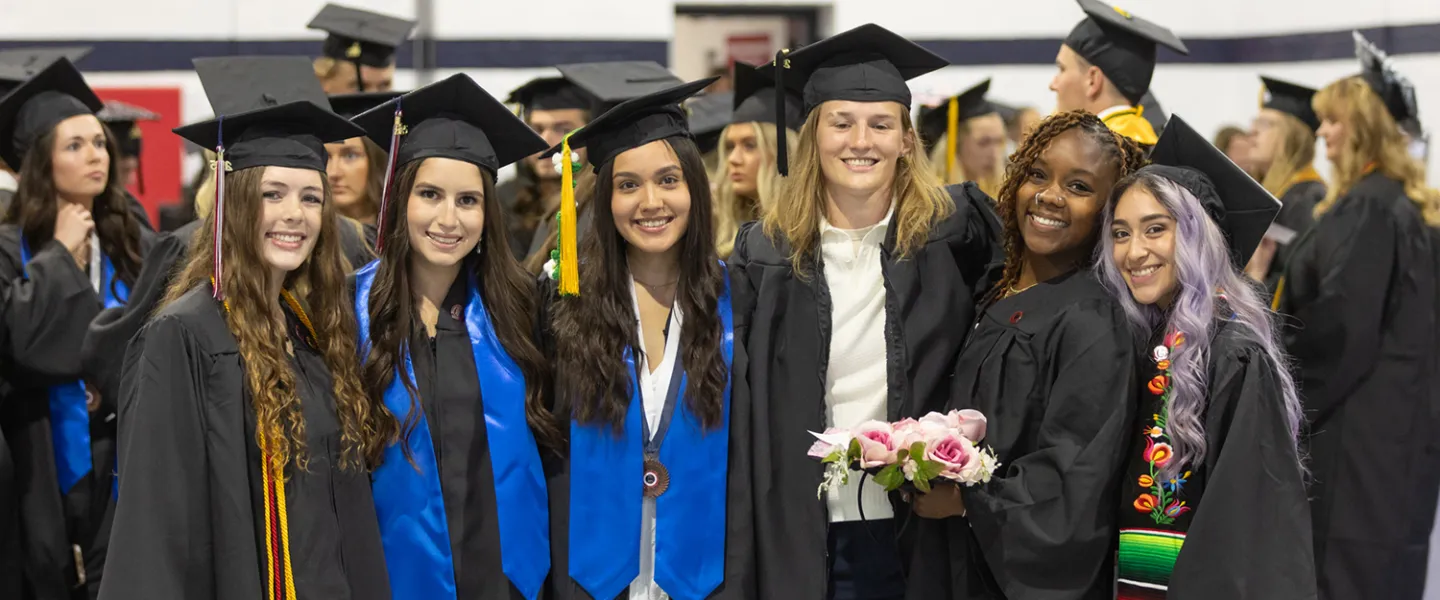 Six female graduates pose in cap and gown following the commencement service. 