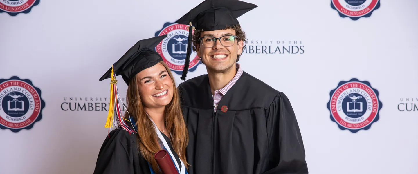 A female and male student pose with their diplomas after graduating. 