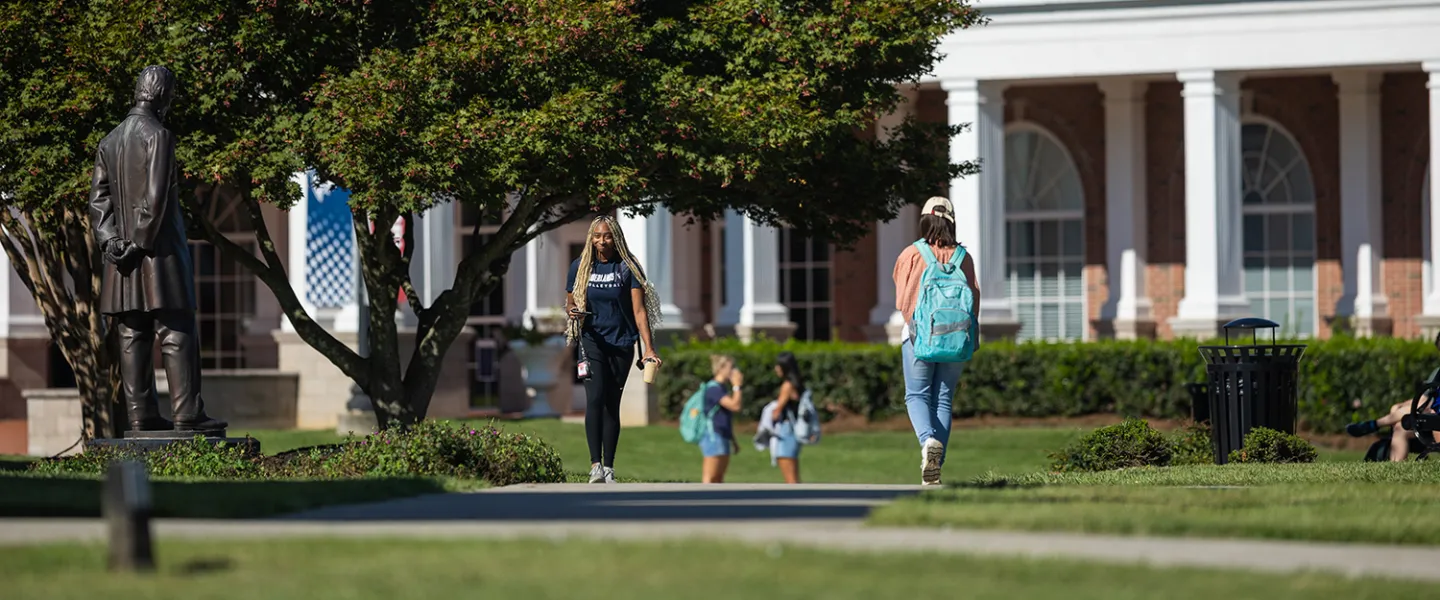 Two students walk on campus near the Lincoln statue. 