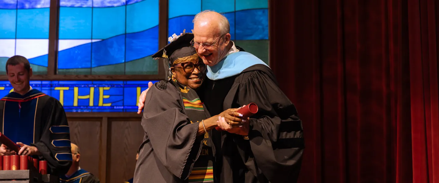 A female graduate hugs the university president after receiving her degree. 