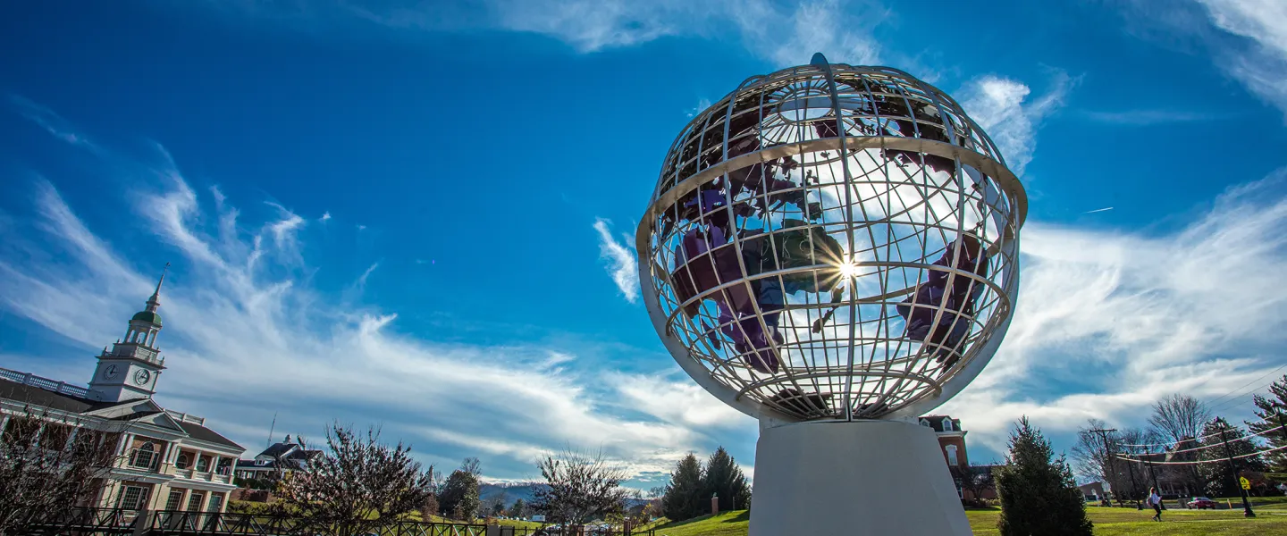 The sun peaks through a statue of the globe on campus. 