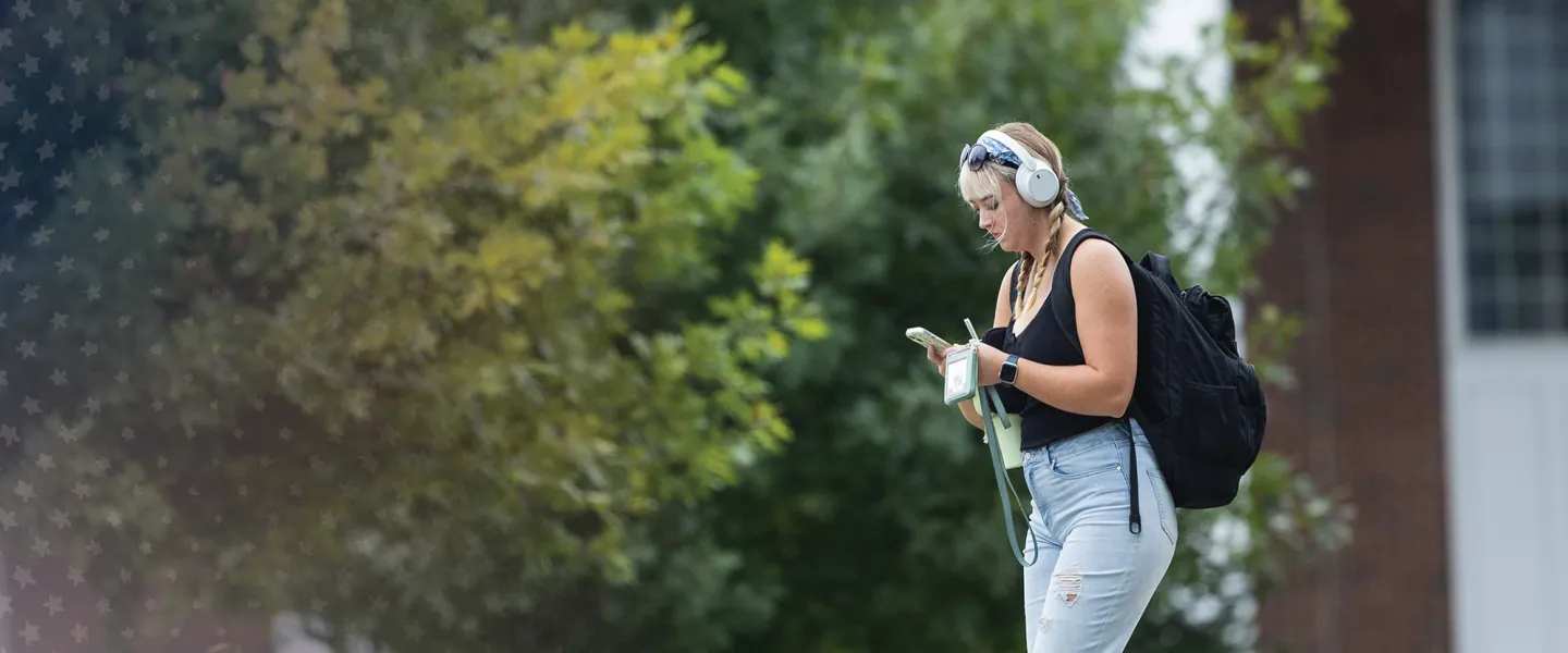 A female student with a backpack looks at her phone after leaving class.