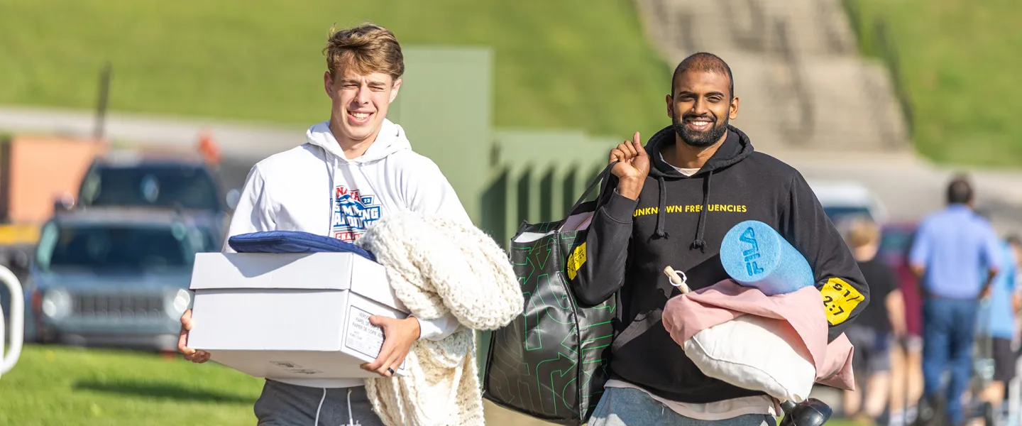 Two male students carry belongings to their dorm on move-in day. 