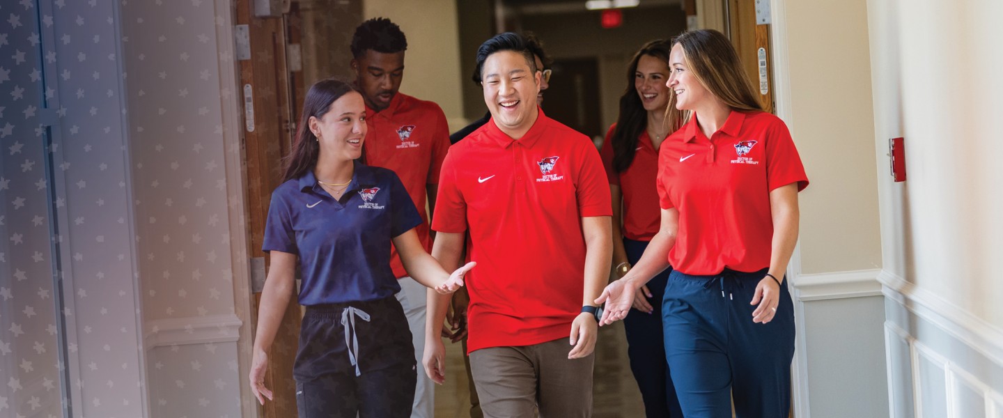 Six physical therapy students walk down a hallway after class. 