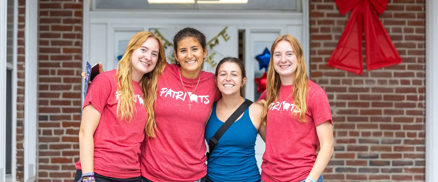 Four female students pose together in front of their dorm on move in day. 