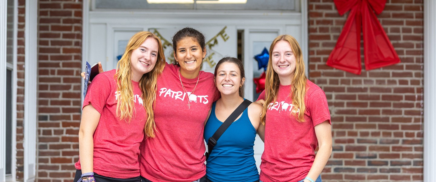 Four female students pose together in front of their dorm on move in day. 