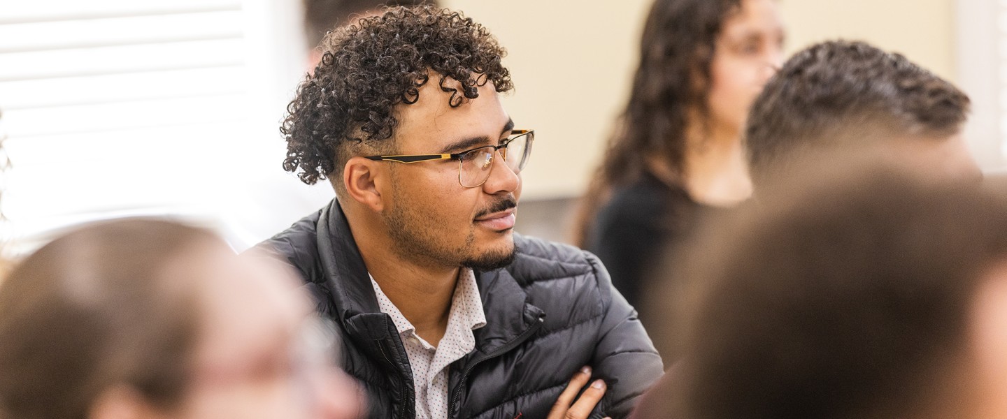 A male student with glasses listens to a speaker during the annual business forum. 