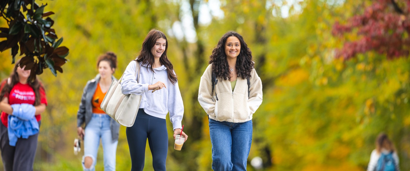 Two female students talk as they walk across campus on a fall morning. 