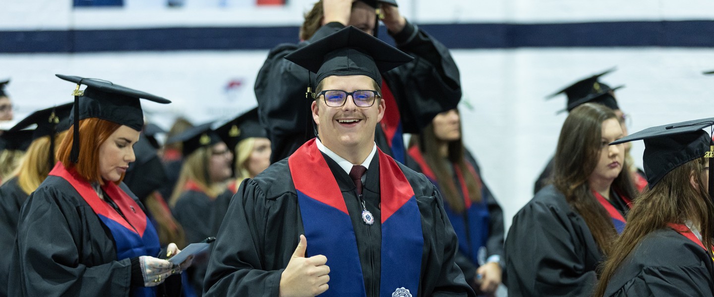 A male honors students gives a thumbs up just ahead of graduation services. 