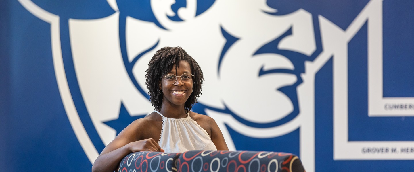A female student sits in a chair in front of a wall with the Cumberlands logo in the student success center. 