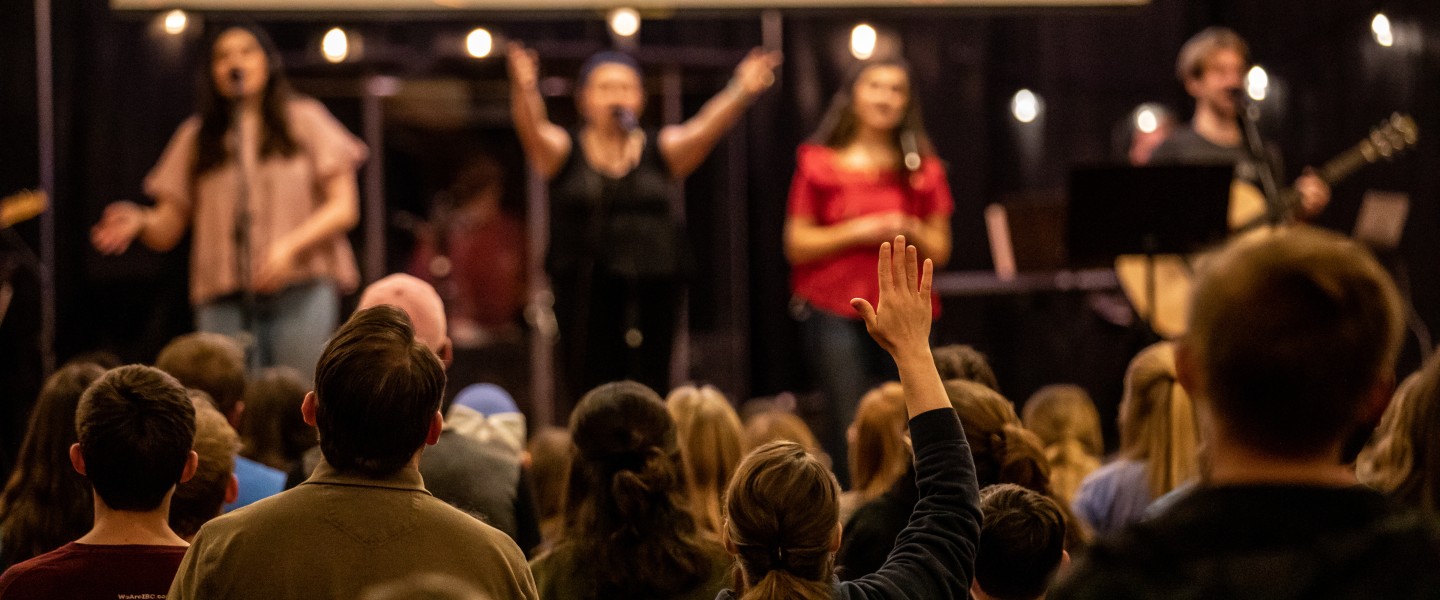 A group of students show praise during a worship event on campus while a band performs. 