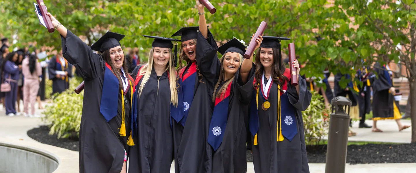 A group of five females in regalia celebrate with their diplomas following commencement services. 
