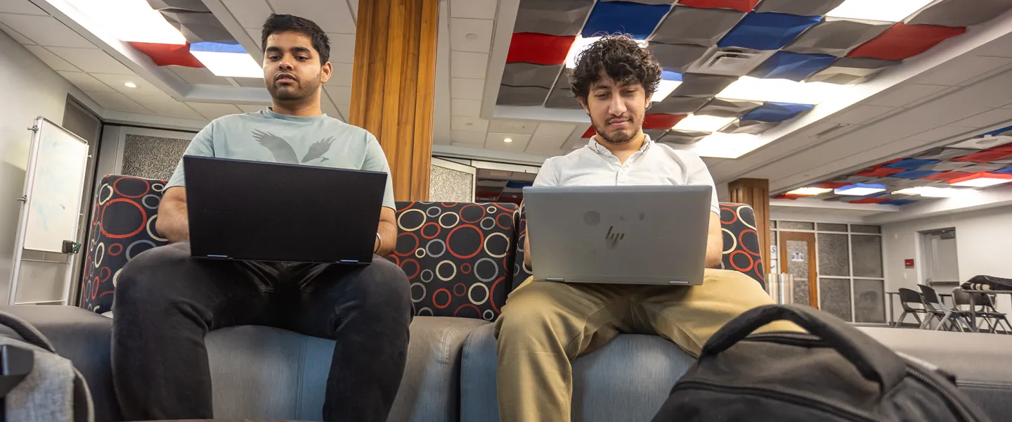 Two male executive students use their computers while in the student success center. 