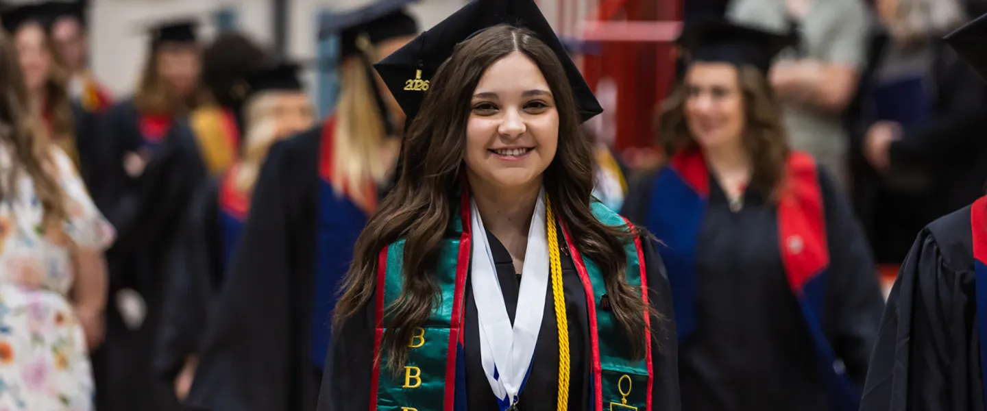 A female student walks with other graduates into the spring graduation ceremony. 
