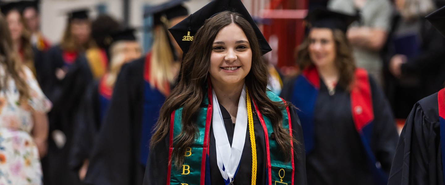 A female student walks with other graduates into the spring graduation ceremony. 
