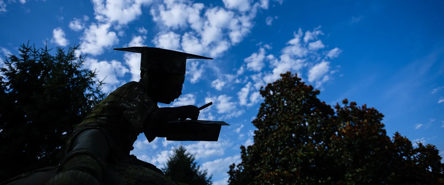 A statue on campus is shaded in the foreground with a dramatic blue sky behind it. 