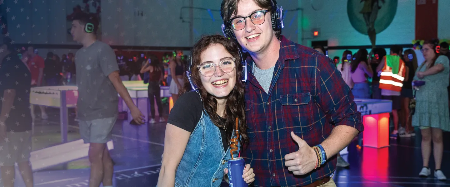 A couple pose for the camera wearing headphones during a dance on campus.