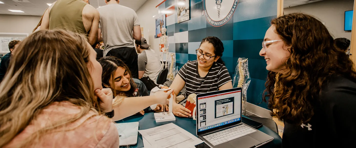 Four female physical therapy students work through a project in the PT lab. 