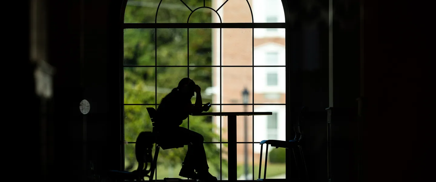 A student is studying in the campus grille but is silhouetted against the window behind her. 