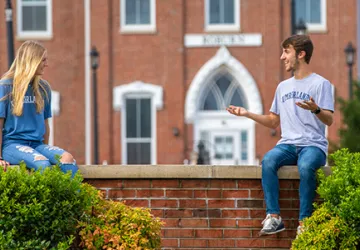 Two students sitting on a wall outside
