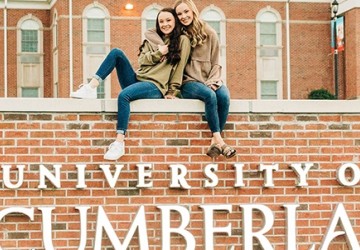 Two students posing for a picture seated on top of the University of the Cumberlands campus sign