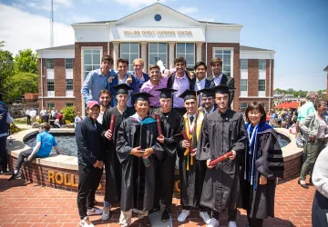 Students wearing cap and gown with friends behind