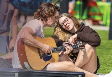 Two students play guitar and sing on campus. 