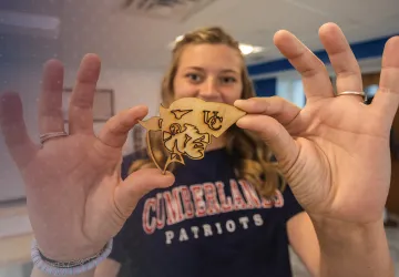 A student displays a woodcraft she made in the library maker space. 