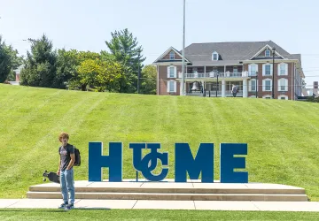 A student stands with a skateboard near Cumberlands HOME sign.