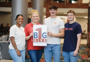 Students hold a sign promoting give day. 