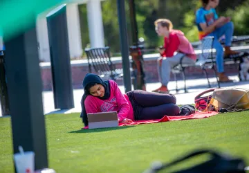 A female student relaxes on campus while using a computer. 
