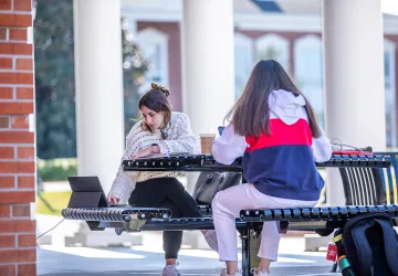 Two girls studying outside on a bench. 
